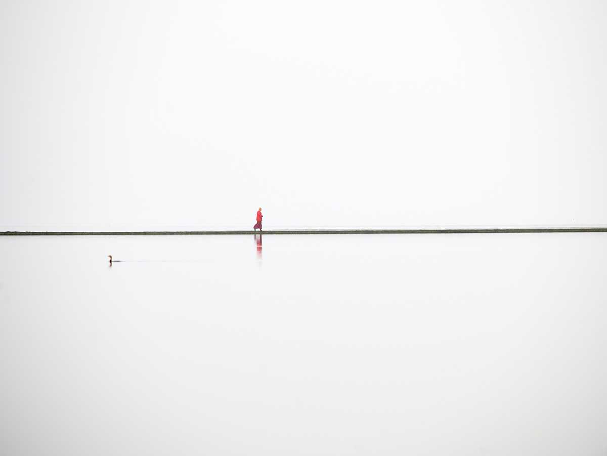 A lone Buddhist monk walks around the boundary wall of the West Kirby Marine Lake.